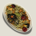 Infusion bio Brise d’été en vrac dans une coupelle blanche : canneberges rouges, morceaux de pomme, feuilles vertes et gousse de cardamome