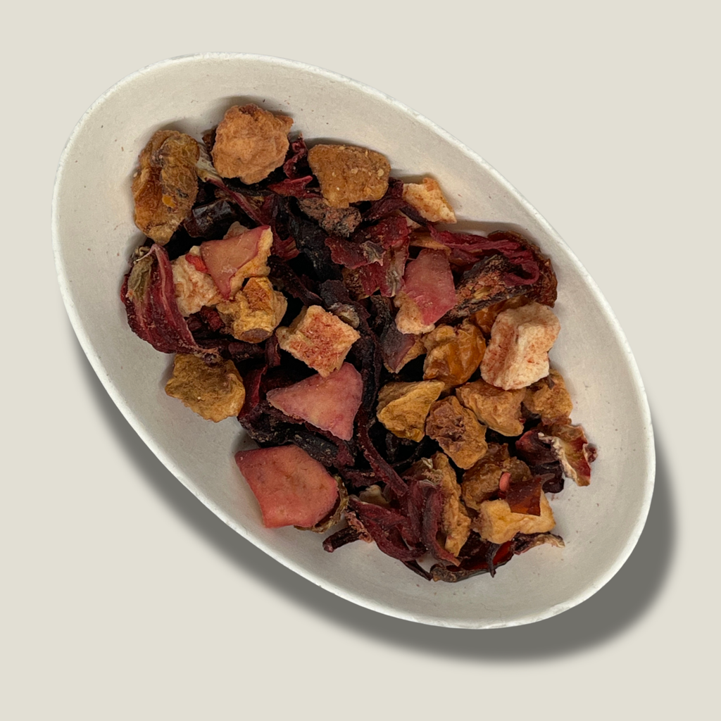 Infusion bio Douceur d’enfance en vrac dans une coupelle blanche : pétales d’hibiscus rouge foncé et morceaux de fruits séchés