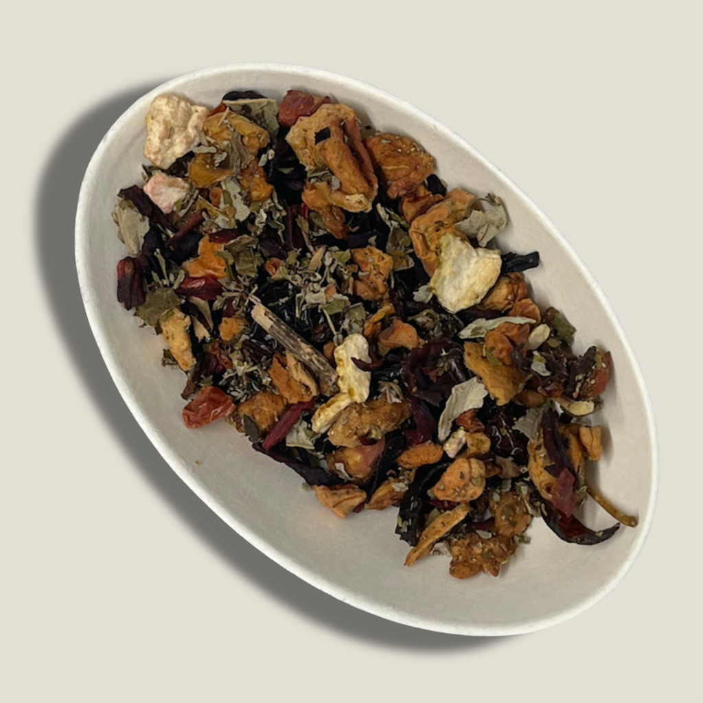 Infusion bio Éclat de grenat en vrac dans une coupelle blanche : pétales d’hibiscus rouge foncé, morceaux de fruits séchés et feuilles vertes