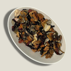 Infusion bio Éclat de grenat en vrac dans une coupelle blanche : pétales d’hibiscus rouge foncé, morceaux de fruits séchés et feuilles vertes