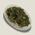 Infusion de plantes bio Équilibre naturel en vrac dans une coupelle blanche : feuilles vertes séchées, graines de fenouil et fruits d’églantier rouge foncé