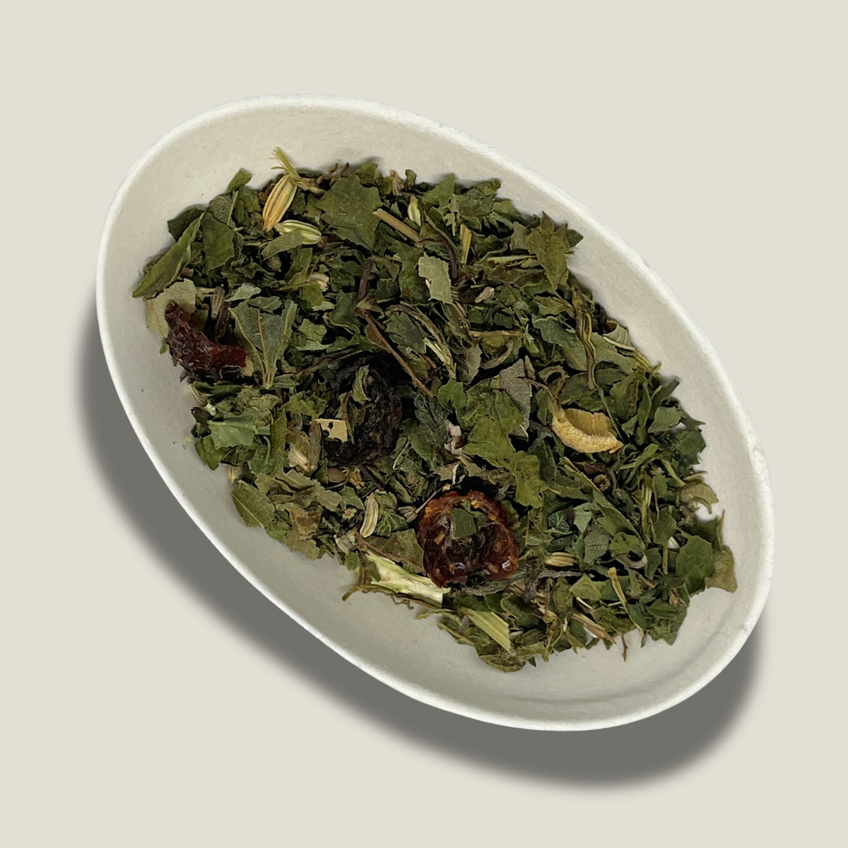 Infusion de plantes bio Équilibre naturel en vrac dans une coupelle blanche : feuilles vertes séchées, graines de fenouil et fruits d’églantier rouge foncé