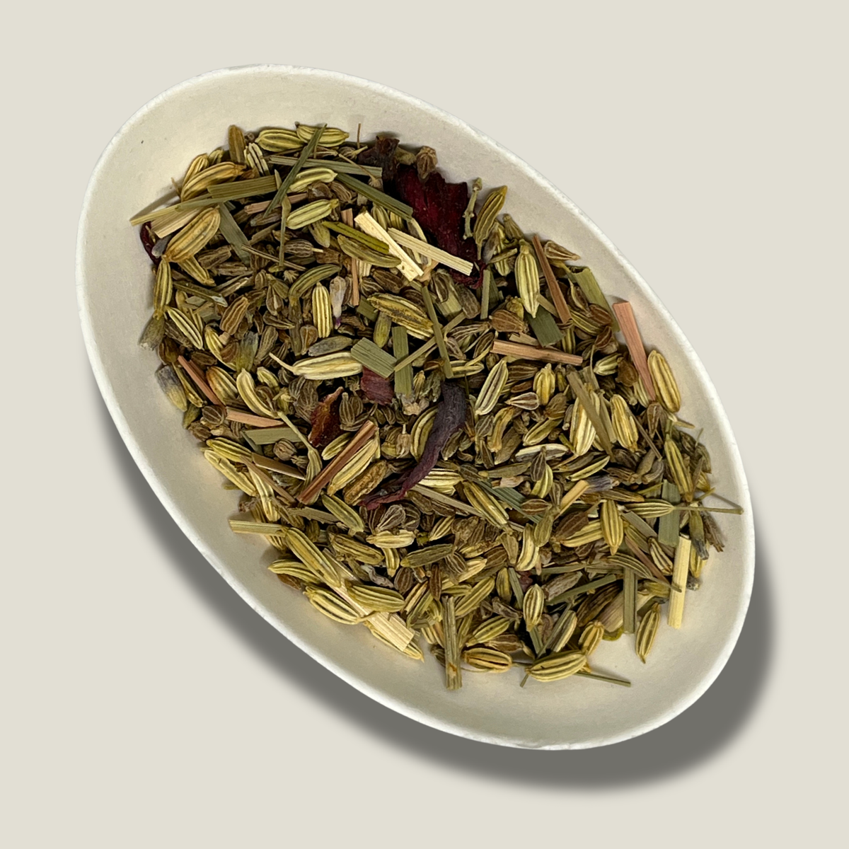 Infusion bio Harmonie anisée en vrac dans une coupelle blanche : graines de fenouil côtelées, brins de citronnelle et pétales d'hibiscus rouge foncé