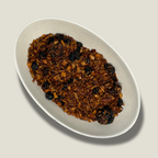Infusion de rooibos bio Velours rubis en vrac dans une coupelle blanche : copeaux de rooibos brun orangé et baies séchées bleu-noir