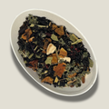 Thé noir bio Éclat d’agrumes en vrac dans une coupelle blanche : feuilles noires, écorces d’orange séchées, morceaux de fruits et feuilles vertes