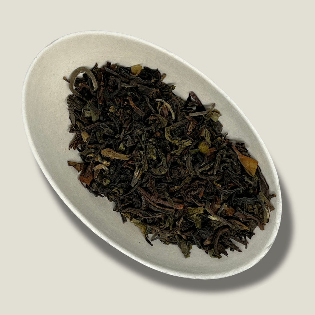 Feuilles de thé Darjeeling FTGFOP1 Chamong bio en vrac dans une coupelle blanche, feuilles torsadées brun foncé et vert olive