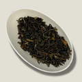 Feuilles de thé Darjeeling FTGFOP1 Chamong bio en vrac dans une coupelle blanche, feuilles torsadées brun foncé et vert olive