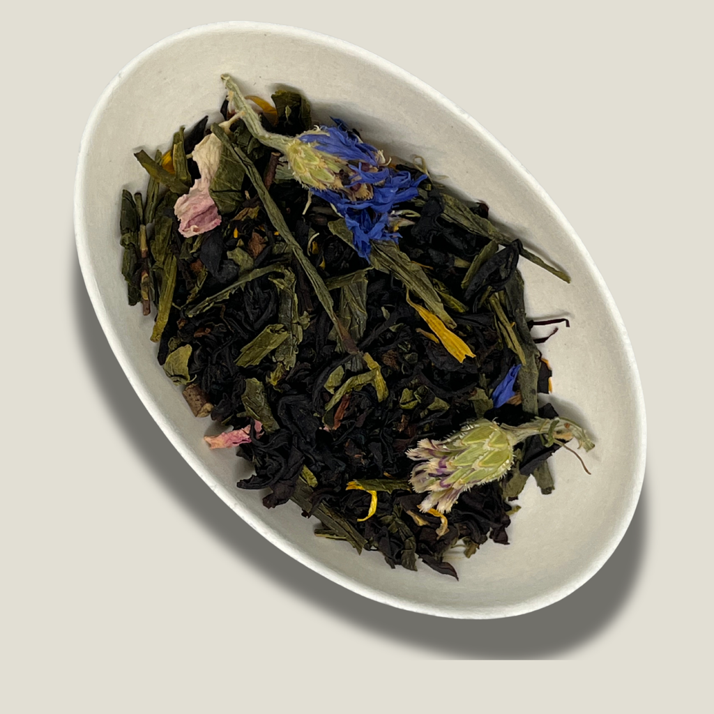 Mélange de thé noir et thé vert bio Évasion tropicale en vrac dans une coupelle blanche : fleurs de bleuet bleues, pétales de rose et pétales de souci jaunes