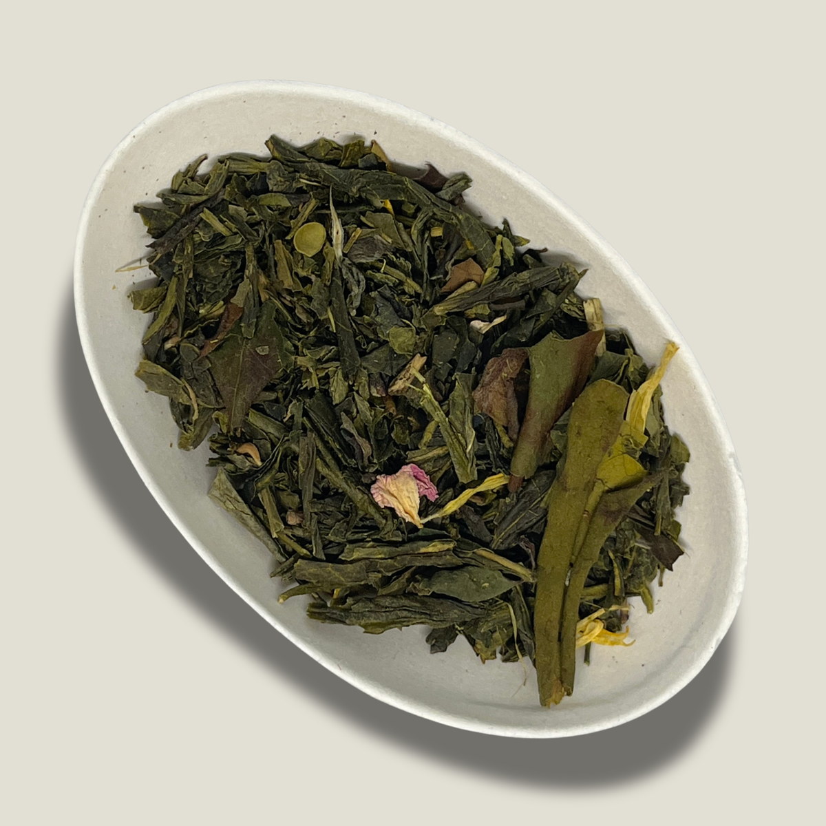 Mélange de thé vert et thé blanc bio Mélodie de l'aube en vrac dans une coupelle blanche : feuilles vertes, un pétale de rose rose pâle, pétales de souci jaunes et grandes feuilles allongées